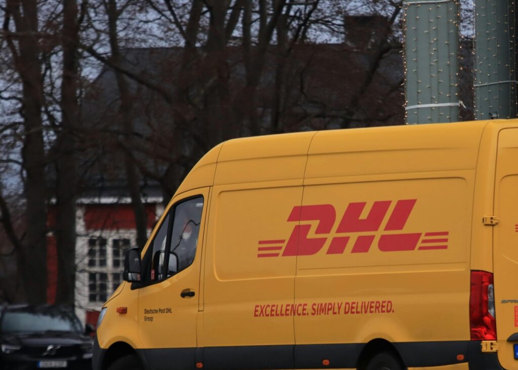Yellow DHL van on street showing company branding and delivery services.